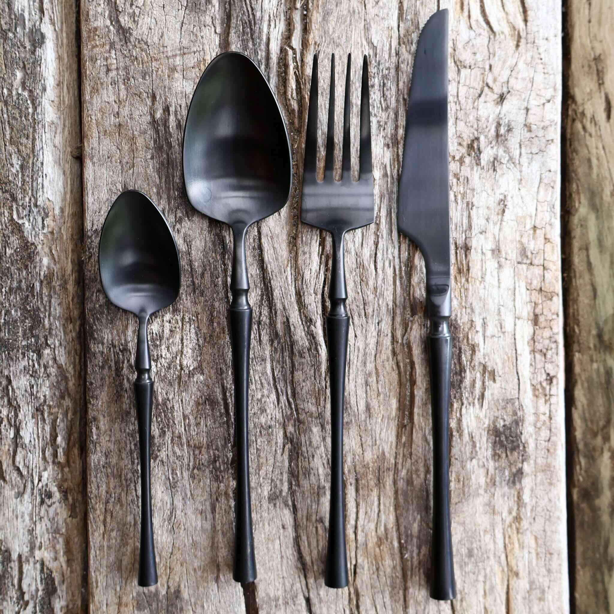 Matte black stainless steel cutlery set with knife fork spoon and teaspoon on wooden table