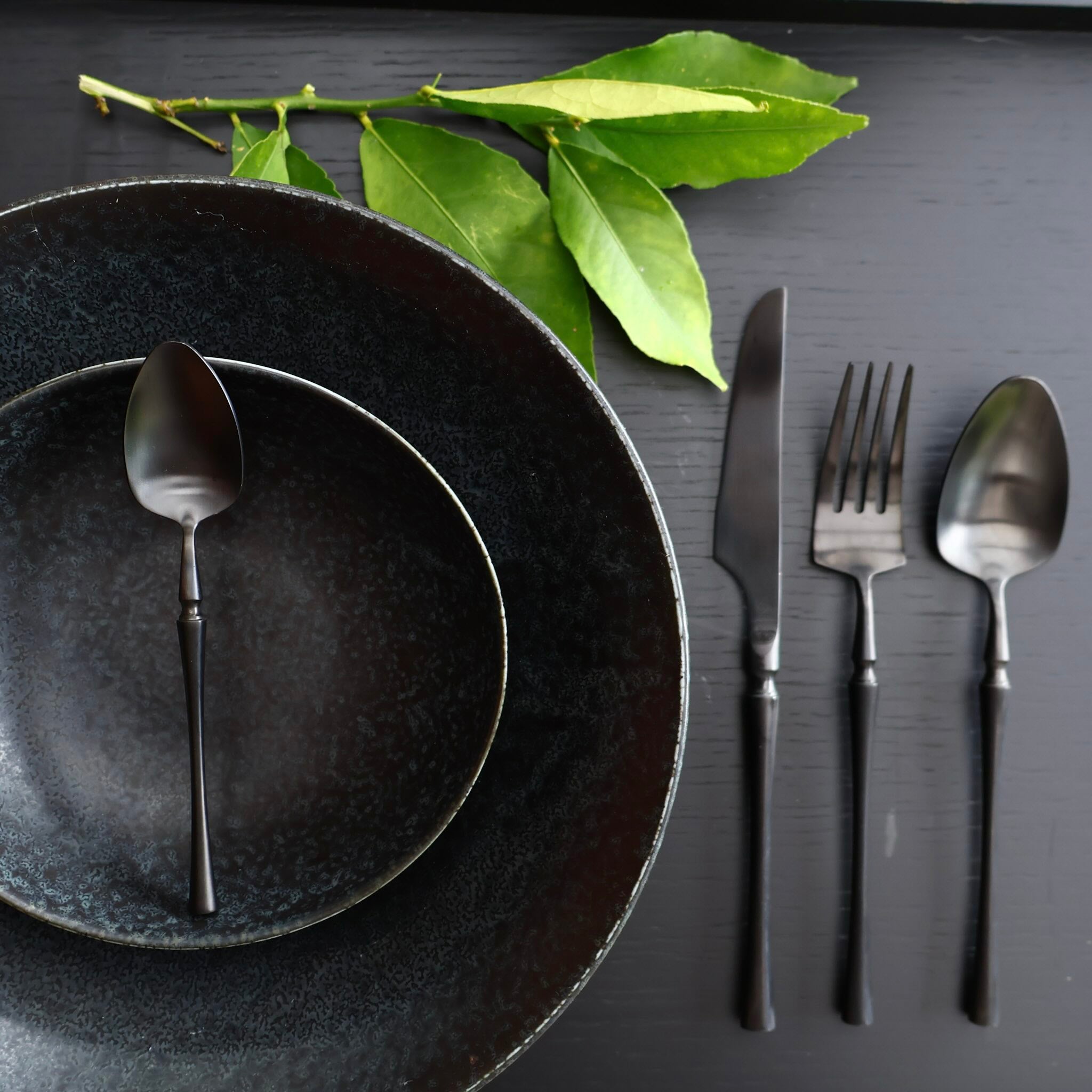 Matte black stainless steel flatware set with modern sculptural design set with dark ceramic plate and bowl