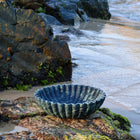 Verde Alpi marble bowl showing natural green stone veining on rocks next to ocean