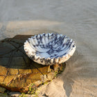 Calacatta Viola marble bowl showing natural marble veining on a beach rock 