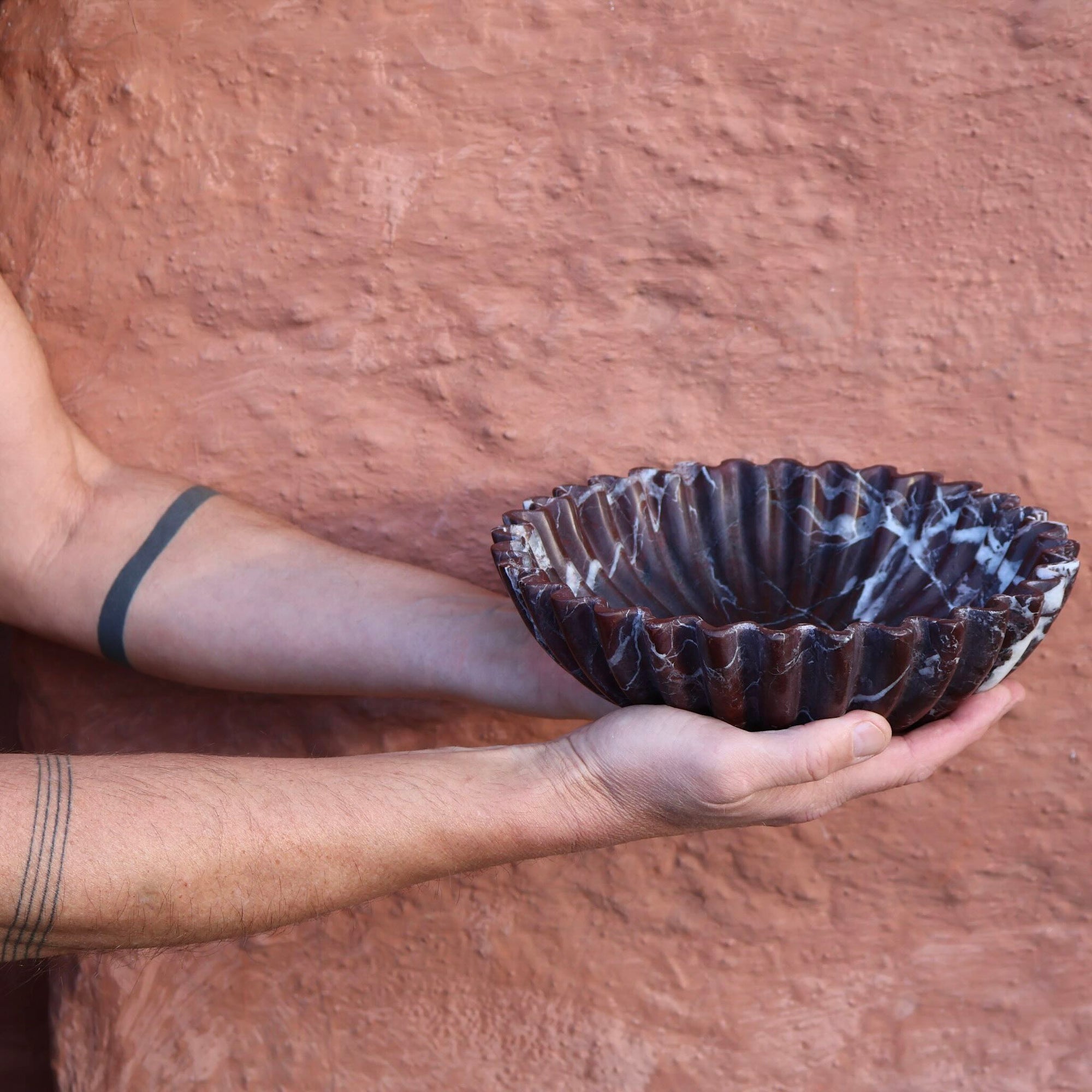 Scalloped edge Rosso Levanto marble bowl carved from natural stone held by man with tattooed arms