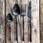 Matte black stainless steel cutlery set with knife fork spoon and teaspoon on wooden table