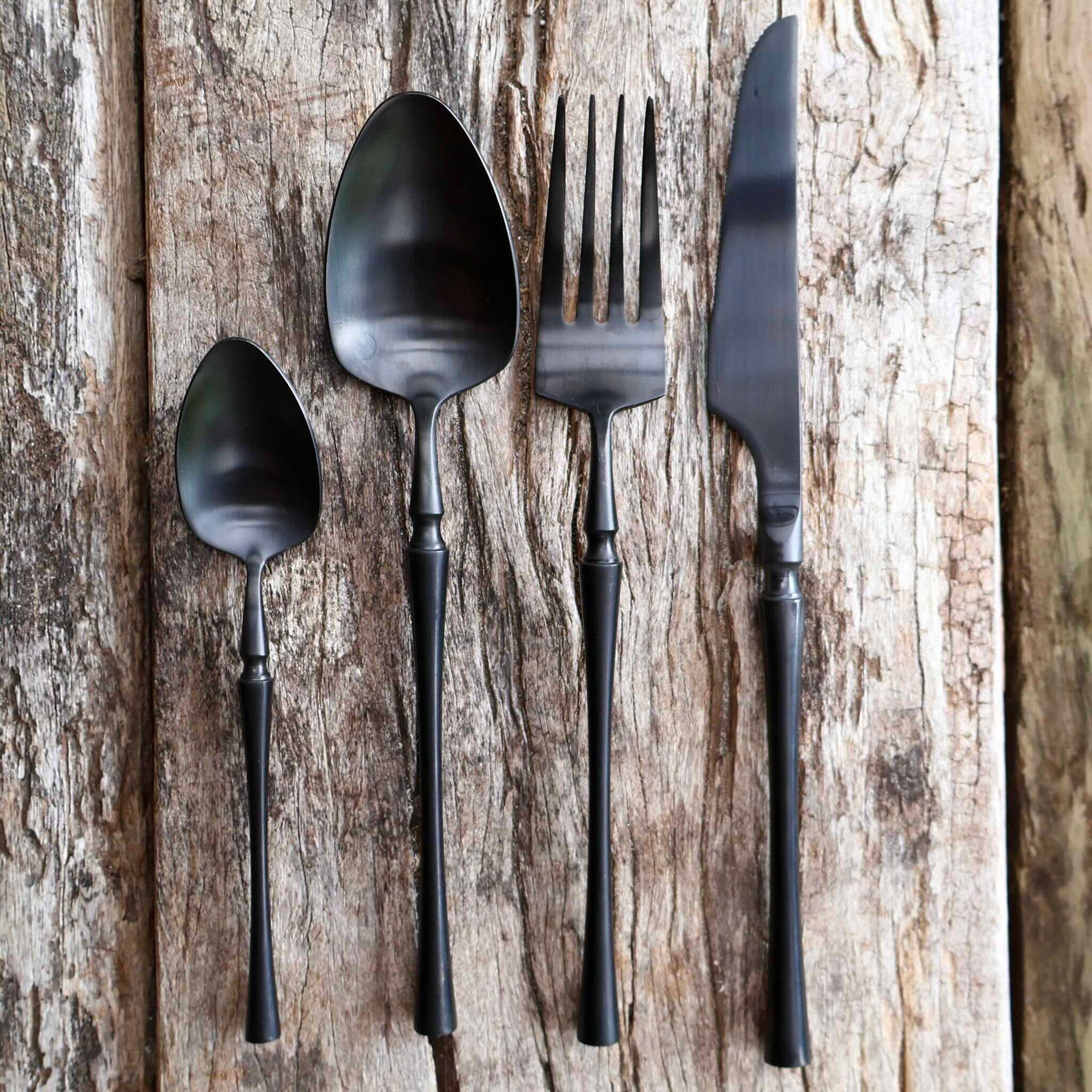 Matte black stainless steel cutlery set with knife fork spoon and teaspoon on wooden table