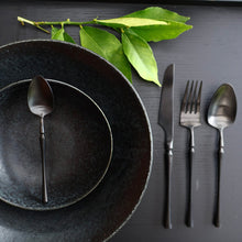 Matte black stainless steel flatware set with modern sculptural design set with dark ceramic plate and bowl