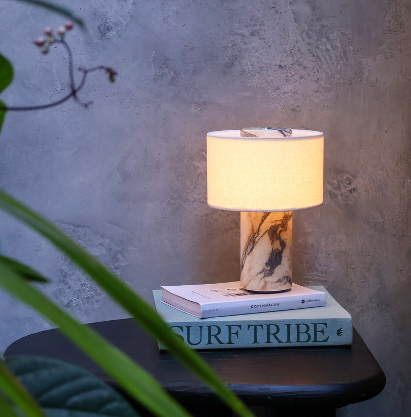 Illuminated cordless table lamp with a sculptural Calacatta Viola marble base, warm fabric shade and distinctive burgundy veining.